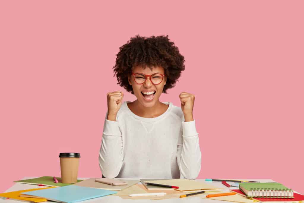 Woman sitting at her desk excited to follow powerful goal setting tips to help her find clarity, take aligned action, and achieve her goals