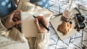 Woman sitting with latte and book with journal prompts for self growth and self improvement